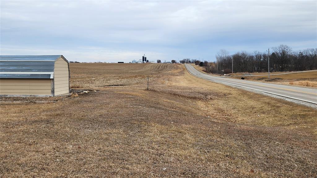 Exterior-6 Rural landscape with a road curving through open fields. A small, shed-like structure is on the left. The fields are brown, suggesting late autumn or winter. Trees line the road in the distance under an overcast sky.