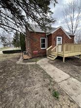 A small red-brick house with a gray roof and light wood porch sits on a patchy yard at 701 S Roche Street, Knoxville IA. A concrete path leads to the porch, with leafless trees in back beneath a cloudy sky—an inviting real estate opportunity.