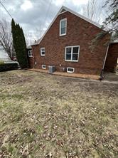 A red brick real estate gem at 701 S Roche Street, Knoxville IA, featuring three windows and an HVAC unit on the side. It’s surrounded by a patchy, leaf-strewn yard with trees and an overcast sky in the background.