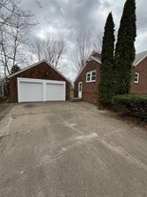 A wide driveway leads to a two-car garage and a brick house at 701 S Roche Street, Knoxville IA, framed by tall evergreens and bare branches beneath a cloudy sky—a perfect spot for your real estate search.