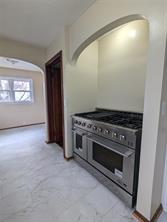 A stainless steel gas range oven is set into a small kitchen nook with arched detail at 701 S Roche Street, Knoxville IA. Light-colored tile flooring and a window are visible in the adjacent room.