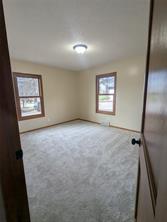 A small, empty room at 701 S Roche Street in Knoxville IA features beige carpet, cream-colored walls, two windows with wooden trim, and a ceiling light fixture, all viewed through a doorway.