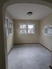 A small, empty room at 701 S Roche Street, Knoxville IA, features beige walls, a white marble-patterned floor, three windows filling the space with natural light, a built-in wall niche on the right, and a centrally placed ceiling light fixture.