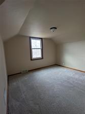 Empty room at 701 S Roche Street, Knoxville IA, featuring beige walls, carpeted floor, a ceiling light, and window with wooden trim. Natural light brightens this real estate gem with a slanted ceiling and baseboard vent.