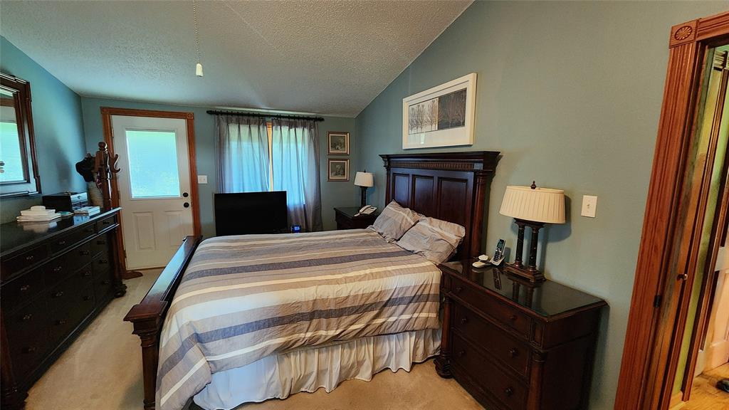 14434 US-65 Acreage 07 A cozy bedroom with blue walls, a large wooden bed with striped bedding, matching nightstands and dressers, a TV at the foot of the bed, a window with sheer curtains, and a door leading outside.