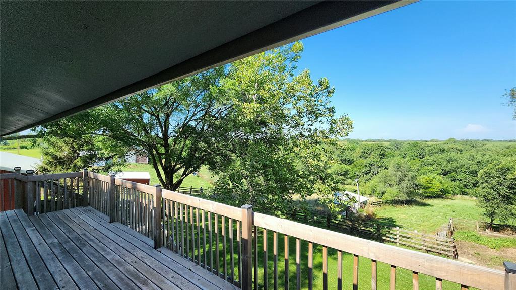 14434 US-65 Acreage 10 View from a wooden deck overlooking a green yard with trees, a fence, and open fields under a clear blue sky on a sunny day.