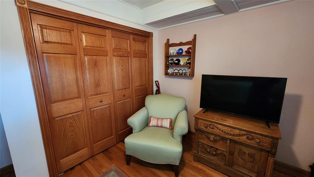 14434 US-65 Acreage 15 A cozy corner with a light green armchair, a striped pillow, a wooden dresser with a flat-screen TV, a wall-mounted shelf holding baseballs, and a double wooden closet door.