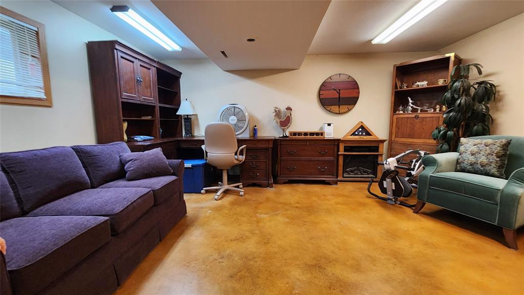 14434 US-65 Acreage 17 A basement room with tan floors, desks, covered furniture, bookshelves, a lamp, a framed painting, and a small window letting in natural light. The space appears tidy and used as an office or lounge area.