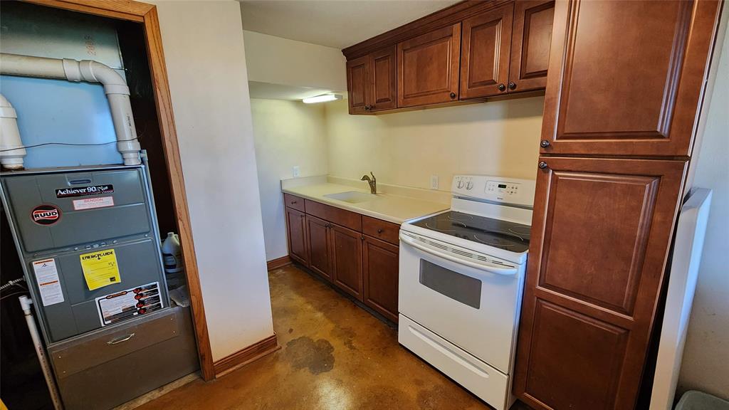 14434 US-65 Acreage 19 A laundry nook with a front-loading washer and dryer, white shelves holding various cleaning supplies, a purple basin, paper towels, and wooden cabinets above with a worn finish.