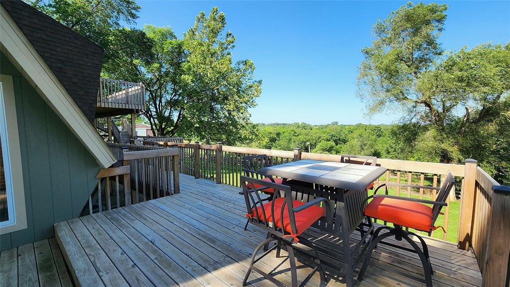 14434 US-65 Acreage 21 A wooden deck with a table and four orange-cushioned chairs overlooks a green yard and trees under a clear blue sky. The deck features a wood railing and nearby house structure.