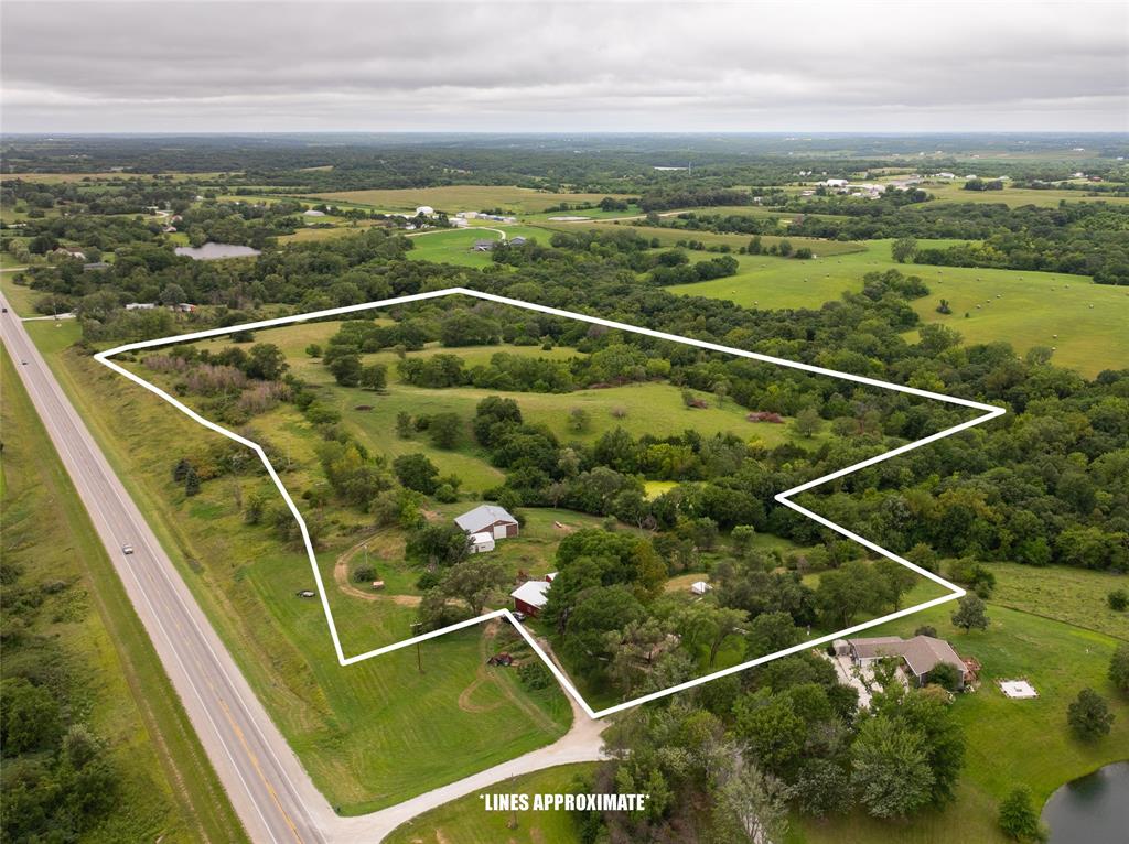 14434 US-65 Acreage 22 Aerial view of a large, tree-filled property outlined in white, located beside a highway, surrounded by green fields and scattered houses under a cloudy sky. Text at the bottom reads "LINES APPROXIMATE.