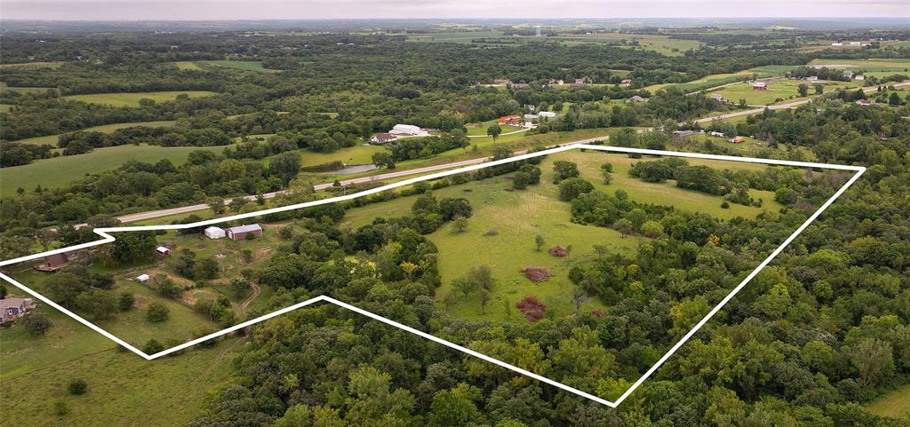 14434 US-65 Acreage 23 Aerial view of a large, green rural property outlined in white, featuring open grassy areas, scattered trees, and a few buildings, surrounded by countryside and nearby roads.