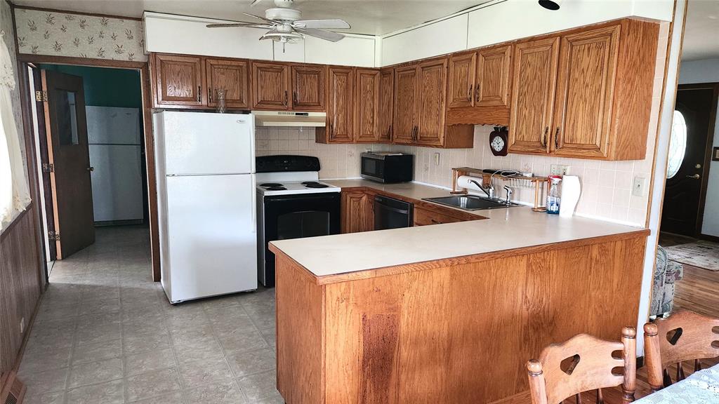 202 E Main St 05 A kitchen with wooden cabinets, white appliances including a refrigerator and stove, a dishwasher, a microwave, and a double sink. There is a wooden dining table with chairs in the foreground.