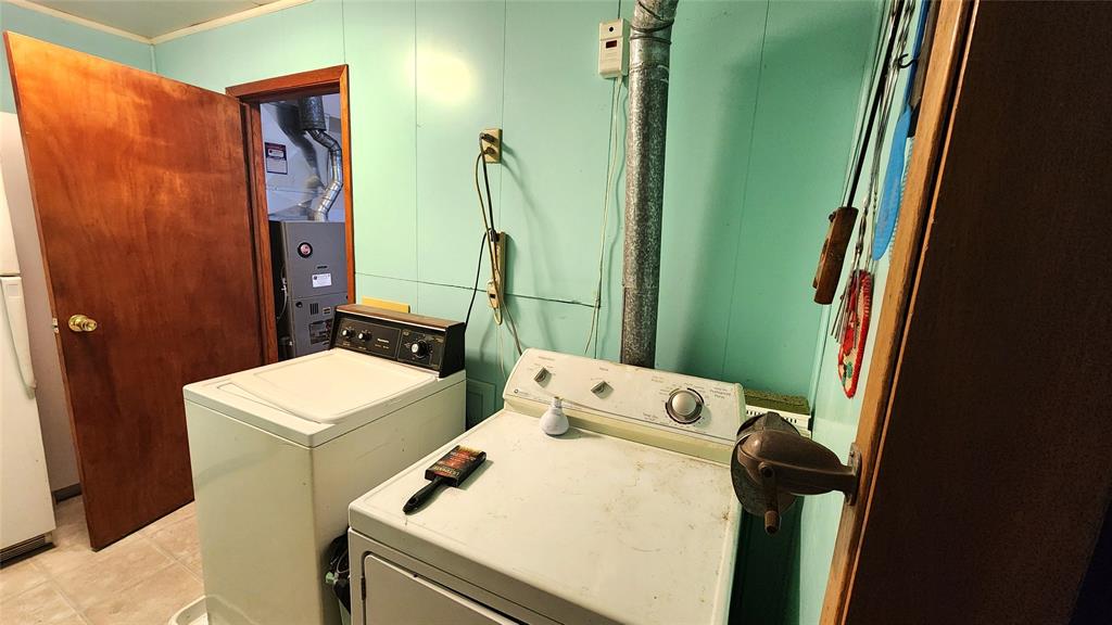 202 E Main St 12 A small laundry room with teal walls, containing a white washing machine and dryer. A paintbrush rests on the dryer. Electrical cords, a vent pipe, and utility equipment are visible, along with an open wooden door.