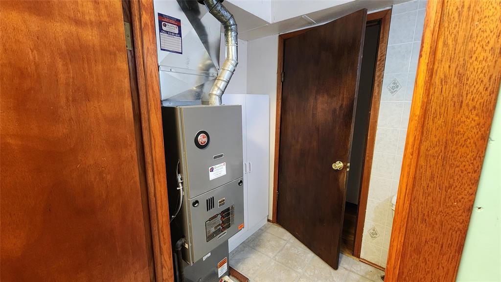 202 E Main St 13 A gray furnace with metal ductwork is installed in a small utility room with wooden doors, tile flooring, and part of a bathroom visible through an open door.