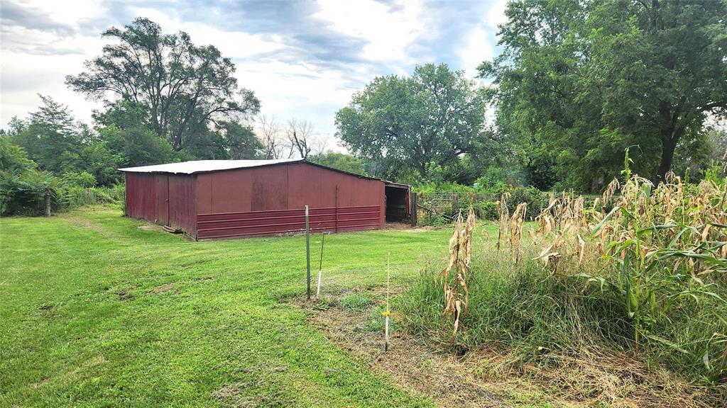 202 E Main St 20 A red barn with a metal roof stands on a grassy plot next to a patch of tall, dry corn and trees under a partly cloudy sky.