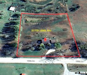 Aerial view of a rural property outlined in red, with a house in the center. The address “21779 120th Ave” is labeled inside the boundary, and 120th Ave runs along the bottom edge of the image.